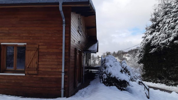 Una cabaña de madera con exterior nevado y un ventanal visible.