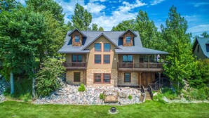 A large, two-story house with a stone foundation, multiple balconies, and a stone retaining wall.