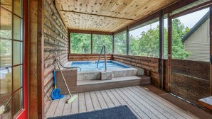 A wooden cabin with a hot tub, wooden deck, and large windows.