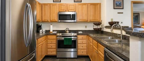 A modern kitchen with stainless steel appliances, wooden cabinets, and a granite countertop.