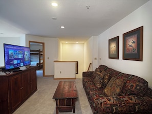 Uma sala de estar com televisão, um sofá estampado, um armário de madeira e um corredor.