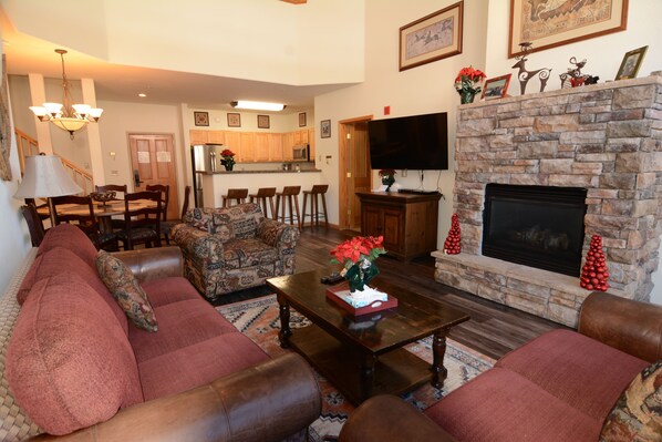 A living room with a fireplace, a dining area, and a kitchen in the background.
