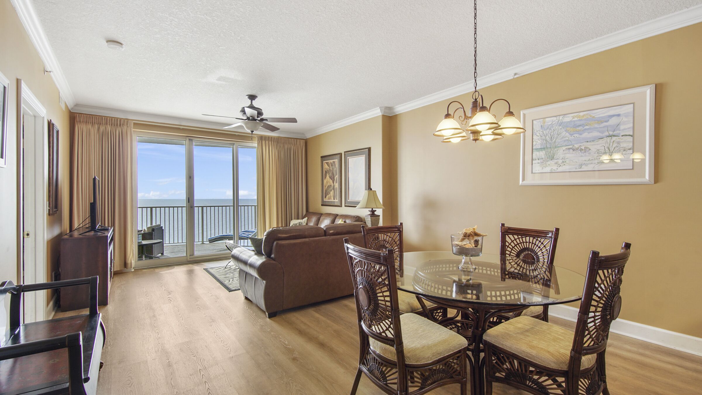 A spacious living area with a balcony, a dining table with chairs, a sofa, and a ceiling fan.