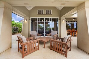 A covered patio area with a wooden table and four chairs, a glass door entrance, and a view of the outdoors. - Luxury, Beachfront- Ka'anapali Beach, Pool & Hot Tub! (Lahaina)