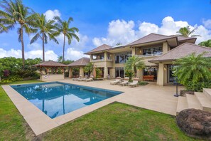 A two-story house with a swimming pool, outdoor seating, and palm trees.