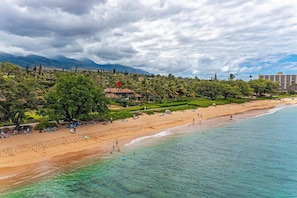 A beach with clear turquoise water, a sandy shore, and a backdrop of mountains and palm trees.