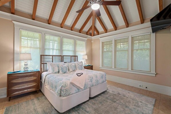 A bedroom with a large bed, wooden headboard, two nightstands, and a ceiling fan.