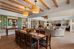 A spacious living area with a dining table, wooden chairs, a sofa, and a staircase leading to an upper level.