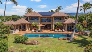 Una casa de dos pisos con piscina, rodeada de palmeras y un jardín cuidado.