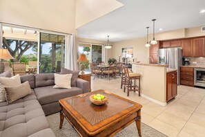 A spacious living area with a sofa, a coffee table with a bowl of fruit, and a dining area with chairs and a table.