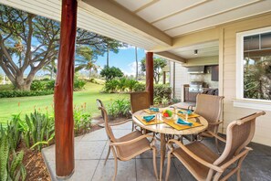 A covered patio with a round table and chairs, a grill area, and a view of a well-maintained garden.