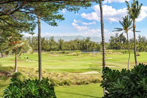 A golf course with palm trees, a clear sky, and a distant view of mountains.