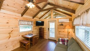 Interior acogedor de una cabaña con paredes de madera, un televisor, un sofá y una mesa de comedor.