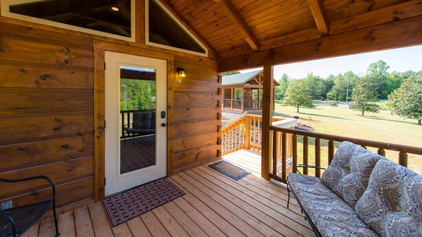 Una cabaña de madera con un porche, una puerta, un banco y vistas a un paisaje verde.