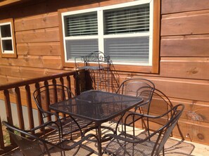 Una baita di legno con un balcone, che include un tavolo e sedie in metallo.