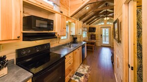 Interior de una cabaña de madera con cocina, que incluye estufa, microondas y lavaplatos.