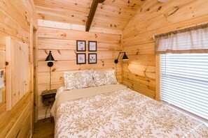 Camera da letto in una baita di legno, con un letto, due lampade a parete e una finestra con persiane.