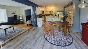 Een ruime woonkamer met een eettafel, stoelen, een televisie en een keuken op de achtergrond.