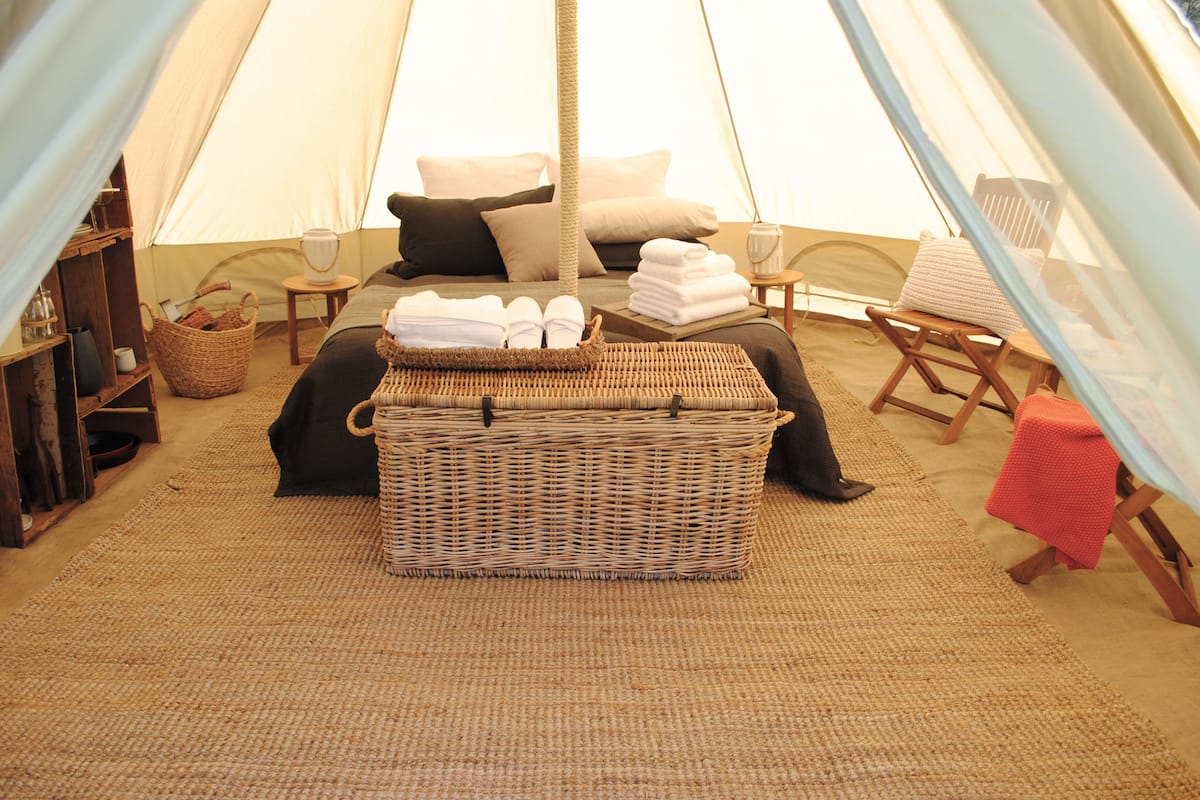 A cozy tent with a bed, pillows, a wicker basket, and a small table.