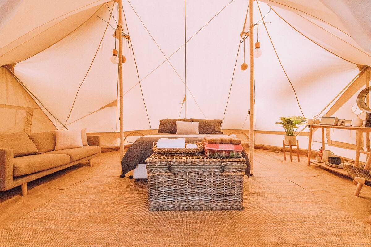 A cozy tented accommodation with a bed, a sofa, and a wicker basket.