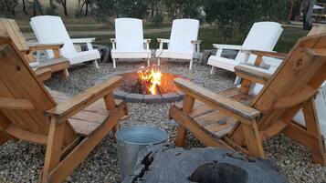 A circular seating arrangement around a fire pit with wooden chairs and a metal bucket.