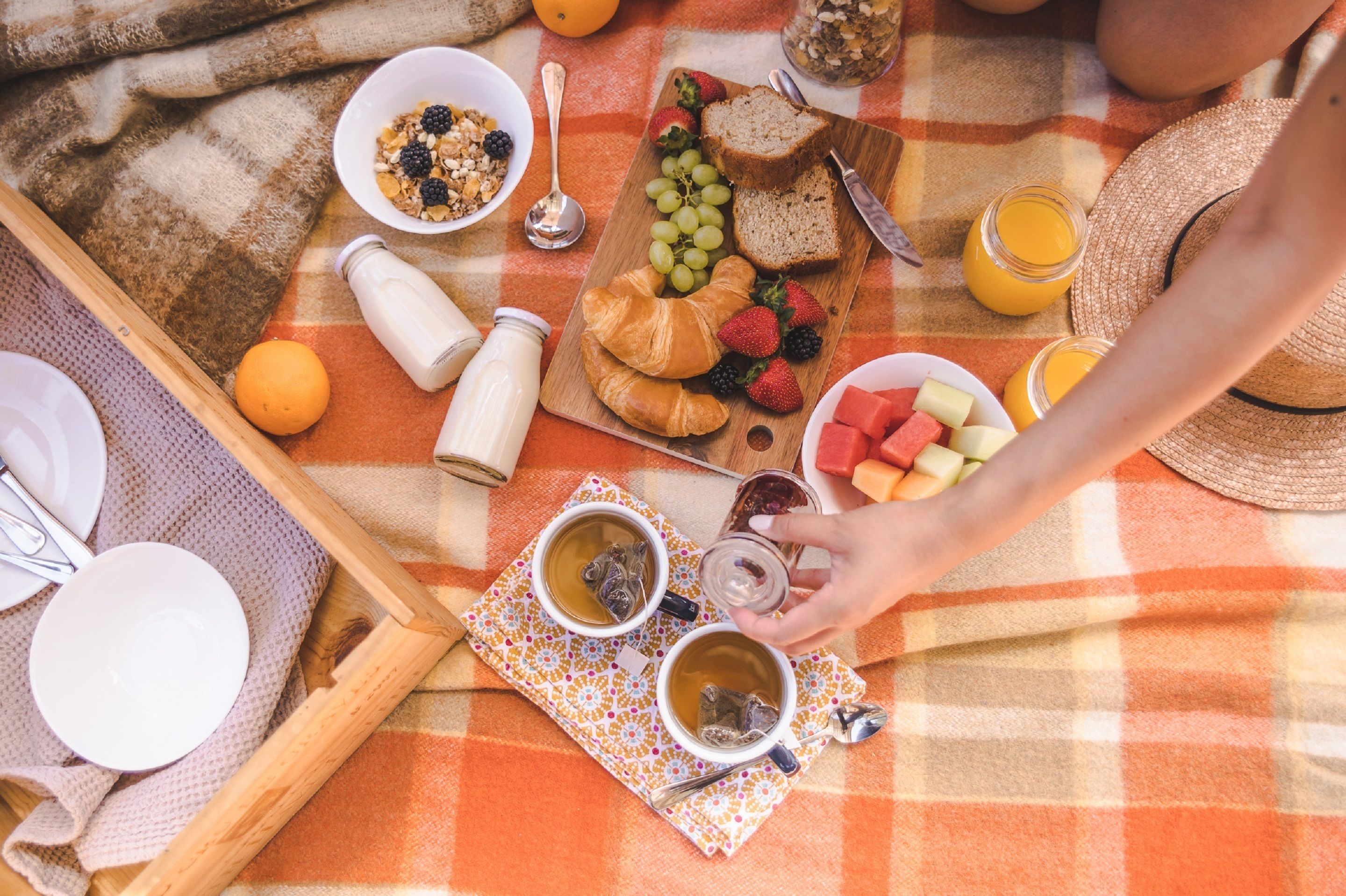 A breakfast setup with croissants, fruits, and beverages on a checkered tablecloth.