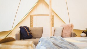 Ein gemütliches Zelt mit einem Bett, Kissen, einem Rucksack und einem kleinen Tisch mit einer Vase.