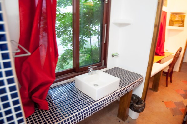 A bathroom with a white sink, red curtains, and a window with a view of trees.