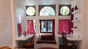 Une pièce comprenant un lit, deux bureaux, des chaises et trois fenêtres avec des rideaux.