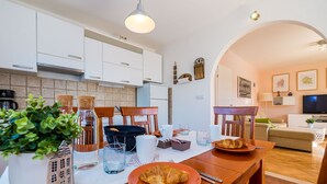 Une cuisine moderne avec des meubles blancs, une table à manger avec deux assiettes de nourriture, et un coin salon confortable avec un canapé et un téléviseur.