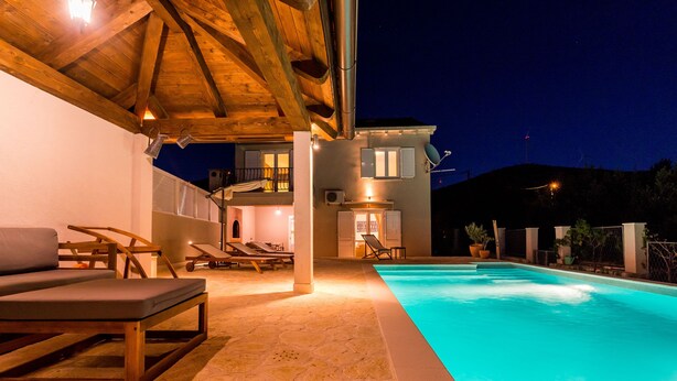 Une piscine avec une terrasse en bois et des chaises longues, un patio couvert et un bâtiment doté de nombreuses fenêtres et d’une antenne parabolique.