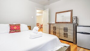 Ett hotellrum med en säng, en byrå i trä, ett kylskåp och en spegel.