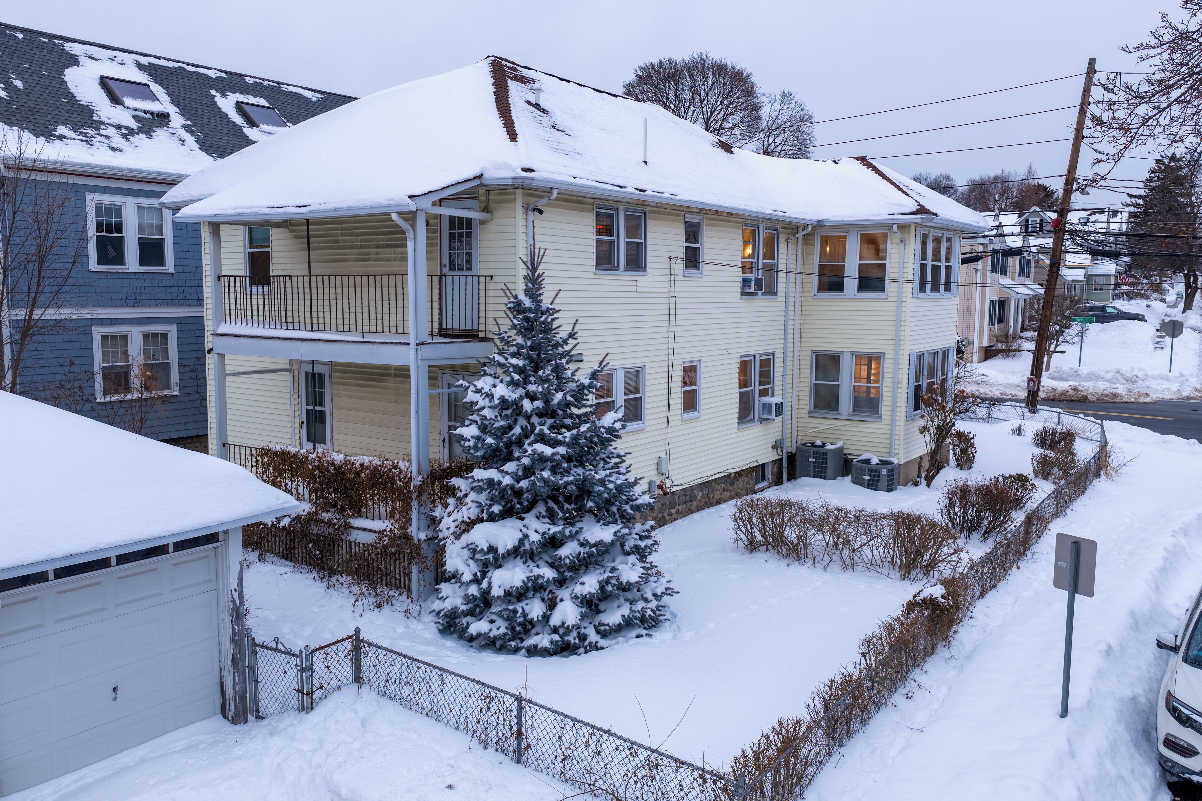 Un immeuble résidentiel de deux étages, dont le toit est recouvert de neige, avec un petit arbre à feuilles persistantes devant.