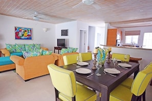 A living room with a sofa set, dining table, and chairs, a television, and artwork on the wall. - Relax Poolside At This Stylish Townhouse - Porters Gate 24 (Porters)