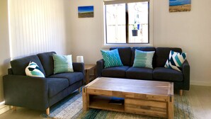 A living room with two dark sofas, a wooden coffee table, and a large window with blinds.
