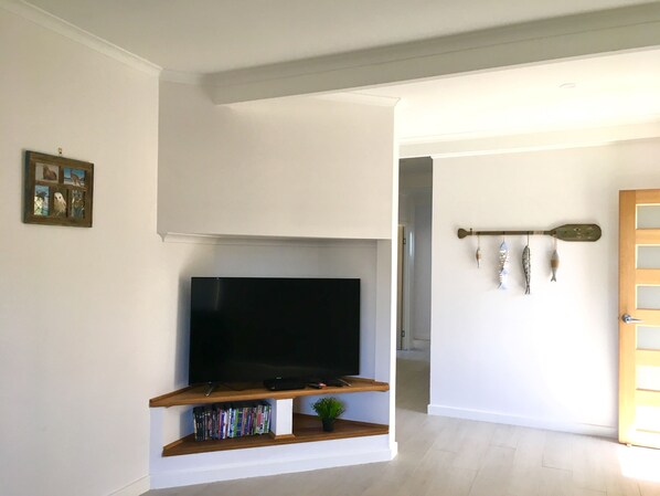 Un salon avec un téléviseur à écran plat posé sur une étagère en bois, une petite plante et un décor mural représentant des poissons.