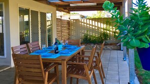An outdoor patio with a wooden table set for dining, surrounded by chairs, and a potted plant.