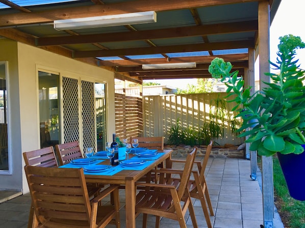 An outdoor patio with a wooden table set for dining, surrounded by chairs, and a potted plant.