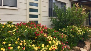 A house with a beige exterior, multiple windows, and a garden with colorful flowers.