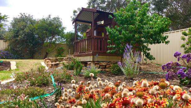 A wooden deck with a small pavilion, surrounded by a garden with various plants and flowers.