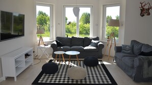 Un saló modern amb un sofà gris, dues taules rodones petites, un moqueta de quadres negres i blancs i un televisor gran de pantalla plana.