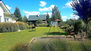 Un jardí residencial amb gespa, un joc de cadira i balancí i un cobert petit.