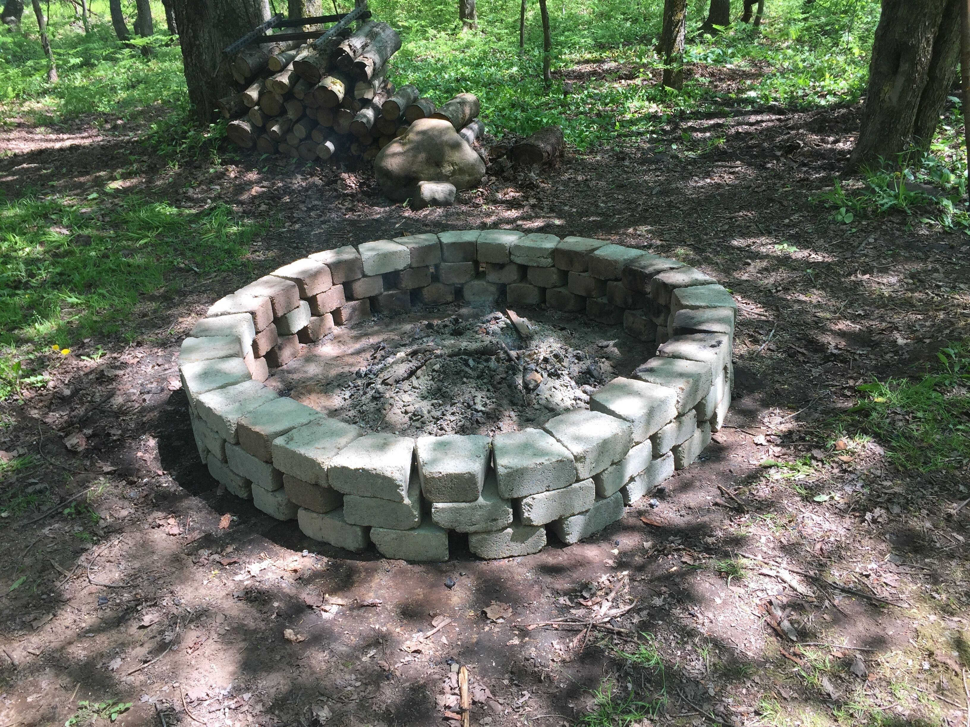 A circular fire pit made of bricks in a forested area.