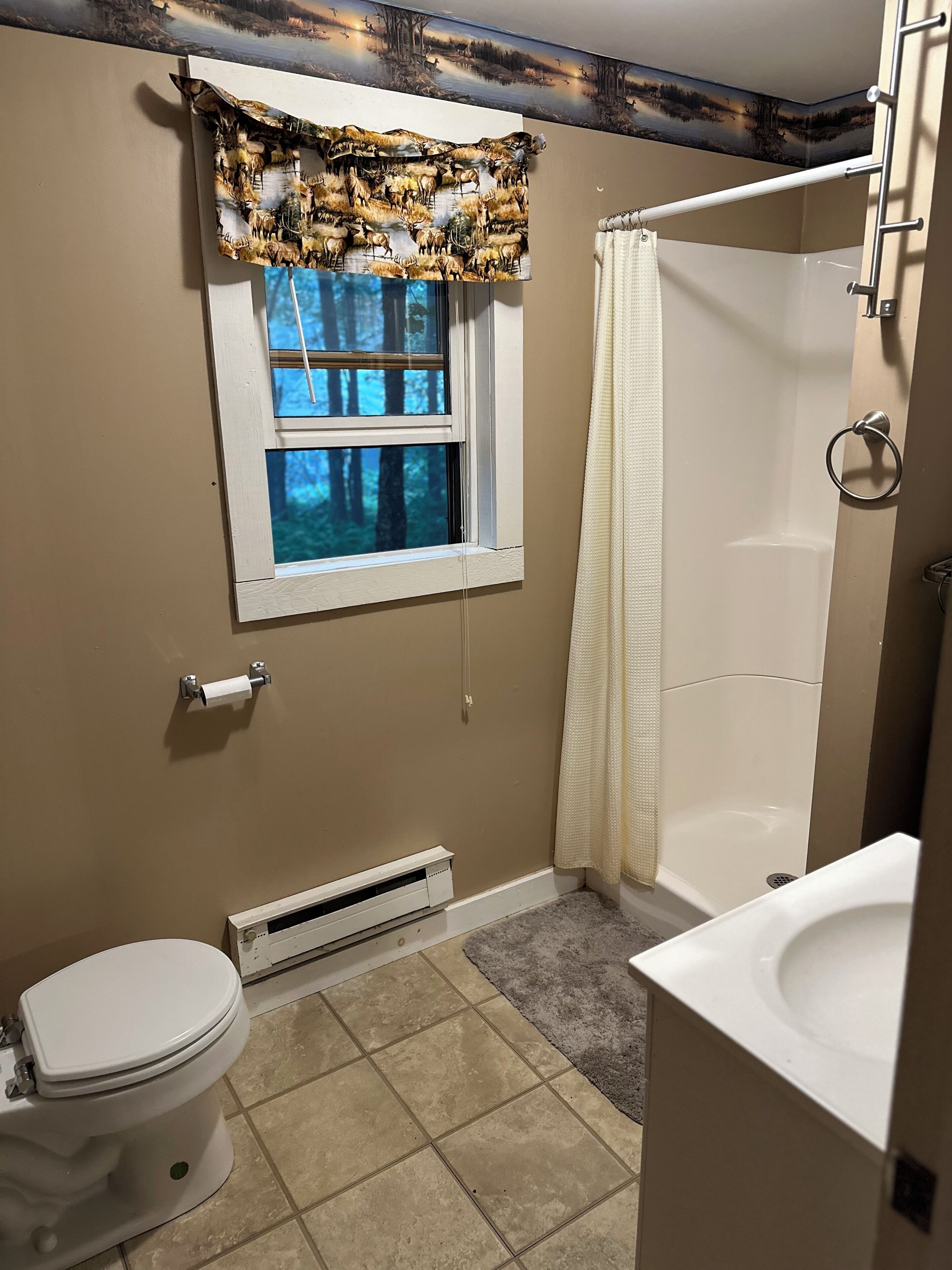 A bathroom with a window, toilet, shower, and sink.