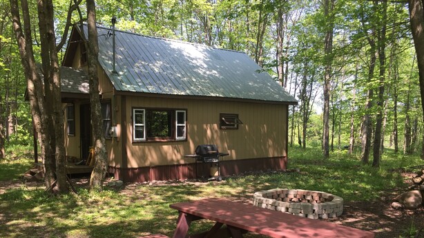 A cabin with a metal roof, a wooden deck, and a stone fire pit.