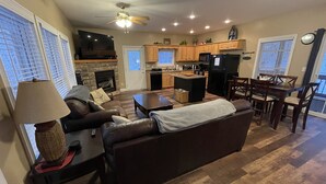 Una sala de estar con chimenea, televisor, sofá, mesa de centro y un comedor con sillas.