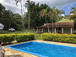 Uma piscina com deck ladrilhado, rodeada por arbustos verdes e palmeiras.