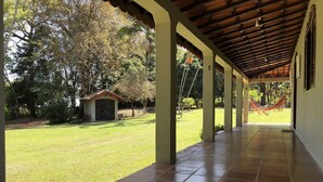 A covered outdoor area with a tiled floor, a small building with a cross on top, and a hammock. - BEAUTIFUL COTTAGE WITH POOL AND LAKE (EXTREMA)