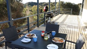 Une table à manger, avec assiettes, couverts et condiments, est installée sur une terrasse offrant une vue sur le paysage environnant.