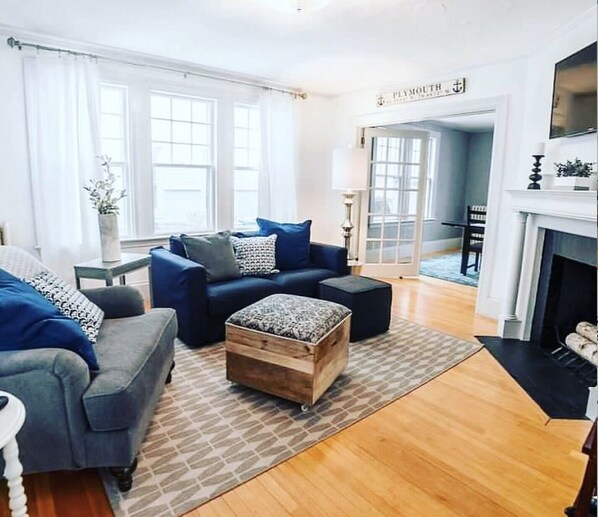 A living room with a blue sofa, a wooden ottoman, and a fireplace.